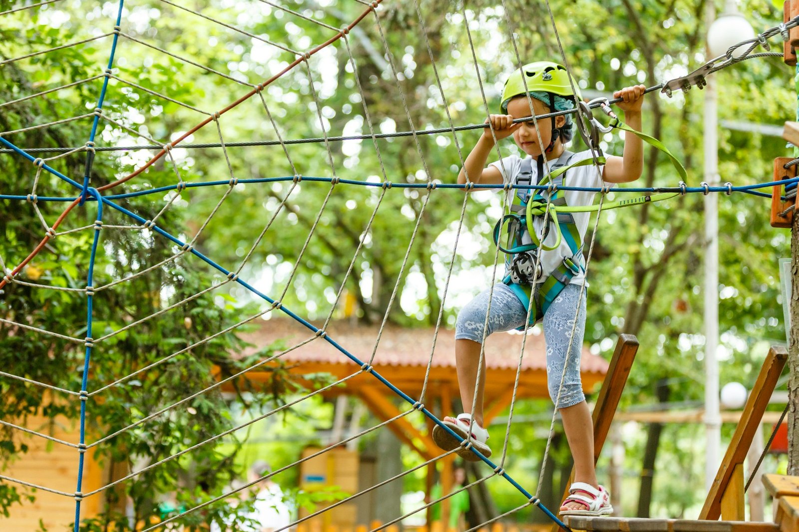 Happy school girl enjoying activity in a climbing adventure park on a summer day