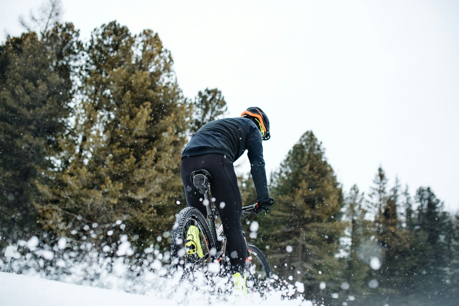 Rear view of mountain biker riding in snow outdoors in winter nature