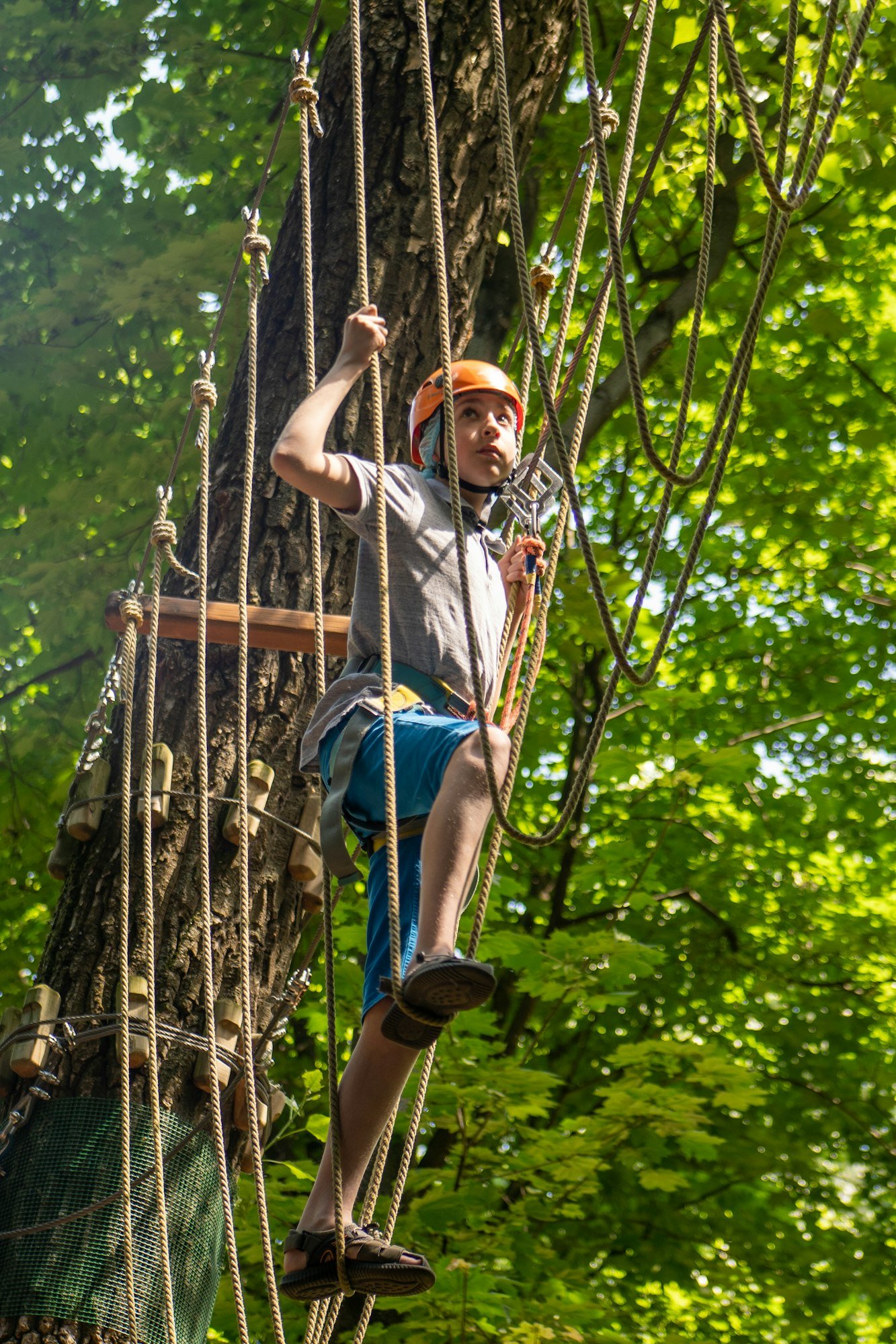 Rope park. A boy teenager in a helmet walks on suspended rope ladders. Carabiners and safety straps